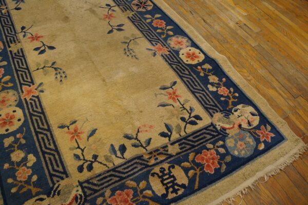 A tan rug with a navy blue border featuring coral flowers and a geometric pattern lies on wood floors.