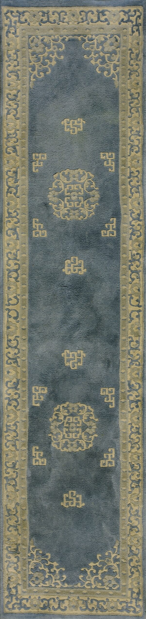 Muted blue runner rug with a wide cream border and low-relief geometric and stylized floral motifs.