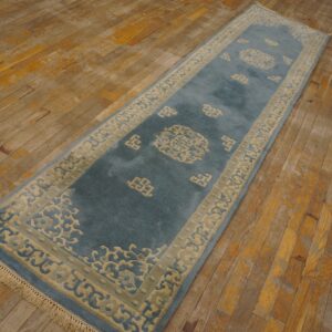 Plush teal and cream runner rug with ornate border patterns lies on heavily worn plank hardwood flooring.