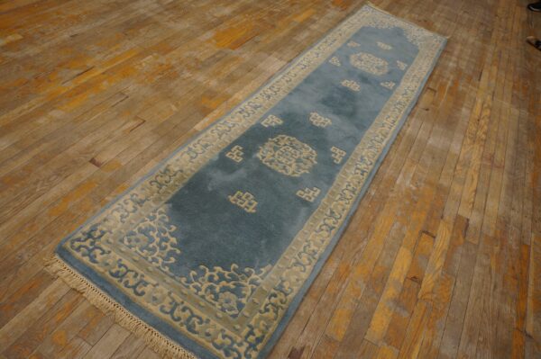 Plush teal and cream runner rug with ornate border patterns lies on heavily worn plank hardwood flooring.