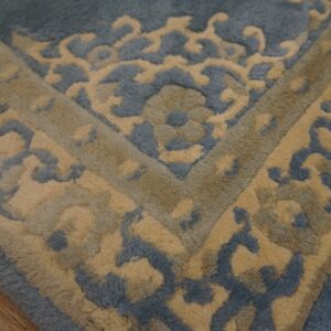 Textured blue and gold high-pile rug detail featuring an ornate scroll pattern on a distressed wood floor.