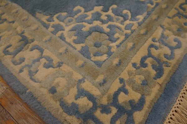 Textured blue and gold high-pile rug detail featuring an ornate scroll pattern on a distressed wood floor.