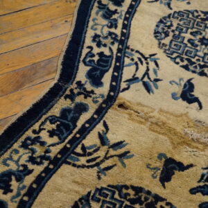 A beige and blue patterned rug with a damaged section exposing shaggy pile lies on a wood floor.