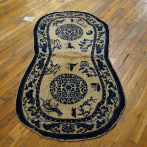 An elongated tan and dark blue patterned rug with circular medallions rests on a scratched wooden floor.
