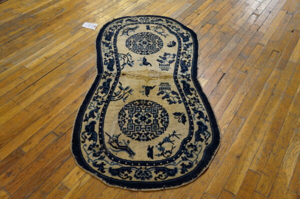 An elongated tan and dark blue patterned rug with circular medallions rests on a scratched wooden floor.