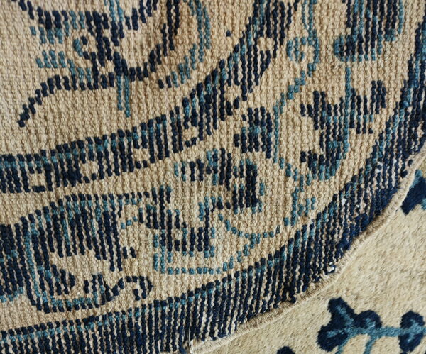 Detail of a tan and blue woven geometric patterned rug meeting a contrasting shaggier cream rug section.