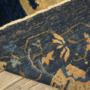 Close-up detail of a folded low-pile blue rug with tan patterns resting on light wood planks.