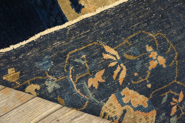 Close-up detail of a folded low-pile blue rug with tan patterns resting on light wood planks.