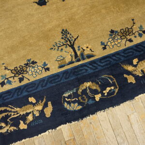 Tan rug field and navy border featuring blue and gold floral and figurative patterns resting on wood planks.