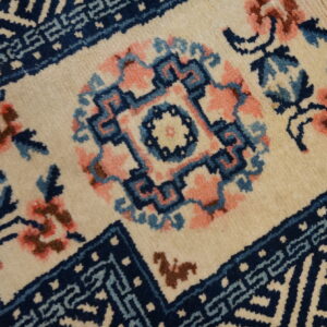 Close-up of a rug with a cream ground, featuring a navy blue geometric medallion and pink floral accents.