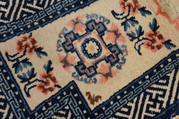 Close-up of a rug with a cream ground, featuring a navy blue geometric medallion and pink floral accents.