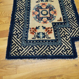 A navy blue and cream rug with geometric borders and pink floral accents rests on light hardwood flooring.