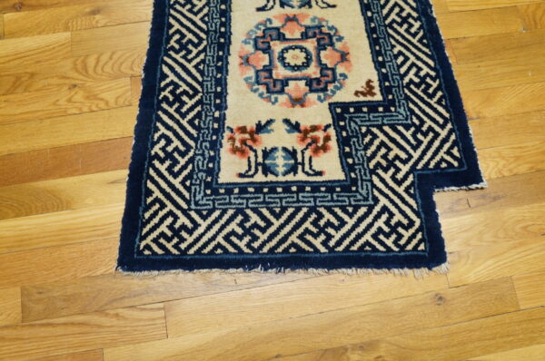 A navy blue and cream rug with geometric borders and pink floral accents rests on light hardwood flooring.