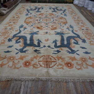 Cream area rug with blue dragon and peach floral borders, lying on weathered wood flooring.