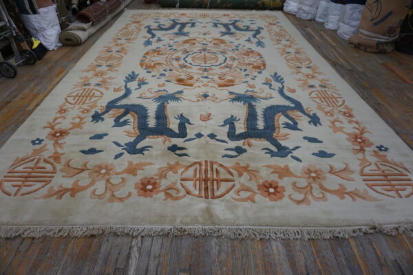 Cream area rug with blue dragon and peach floral borders, lying on weathered wood flooring.