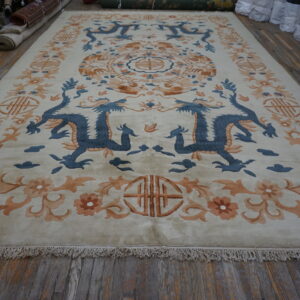 Cream rug with blue dragon and orange floral motifs displayed on rustic wood plank flooring.