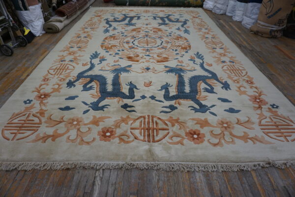 Cream rug with blue dragon and orange floral motifs displayed on rustic wood plank flooring.