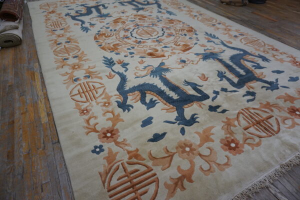 Cream rug with slate blue dragons and orange floral borders displayed on rustic wooden planks.