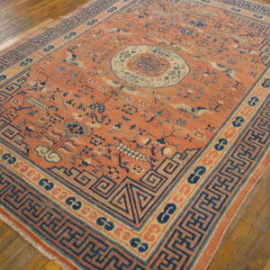Low-pile rug with salmon field, blue fretwork borders, and floral patterns on wood flooring.