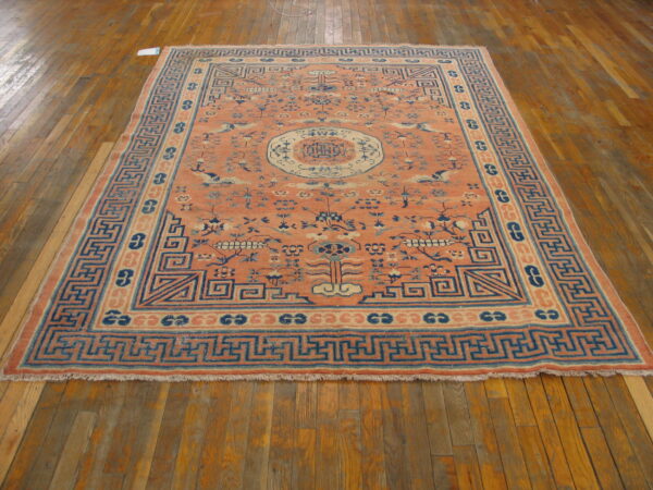 Low-pile salmon and blue rug featuring a central medallion and complex geometric borders on hardwood flooring.