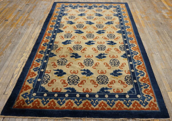 Low-pile rug featuring a cream field, blue medallions, and an orange patterned border on worn wood floors.