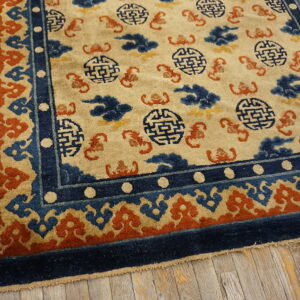 Beige rug featuring navy blue fretwork and orange scroll patterns, bordered in deep blue, on aged wooden planks.