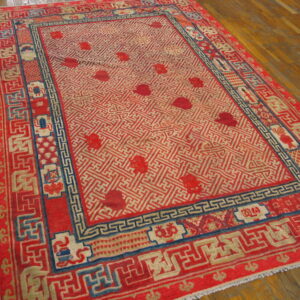 Red rug with detailed blue and cream geometric borders surrounds a trellis patterned field on wood flooring.