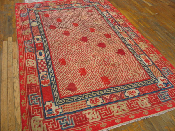 Red rug with detailed blue and cream geometric borders surrounds a trellis patterned field on wood flooring.