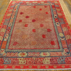 Red and tan geometric rug with blue accents and multiple borders lies on a polished wood floor.