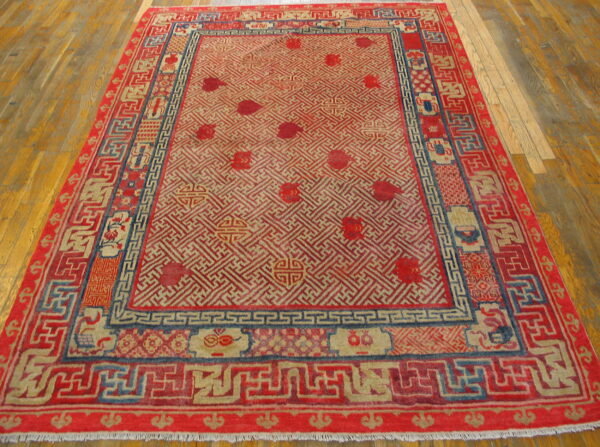 Red and tan geometric rug with blue accents and multiple borders lies on a polished wood floor.