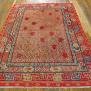 Red area rug with a tan geometric trellis field and detailed borders on hardwood flooring.
