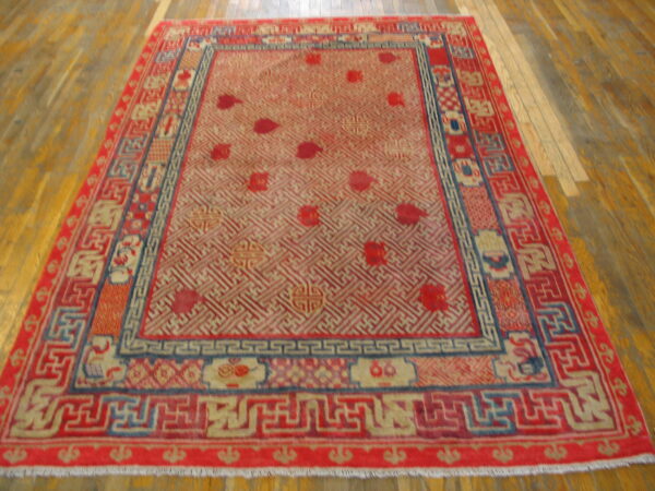 Red area rug with a tan geometric trellis field and detailed borders on hardwood flooring.