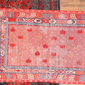 Red and cream rug featuring a dense geometric fretwork pattern and complex blue borders on wood flooring.