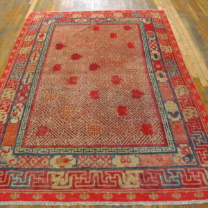 Red, beige, and blue traditional rug featuring intricate geometric lattice patterns on light wood flooring.