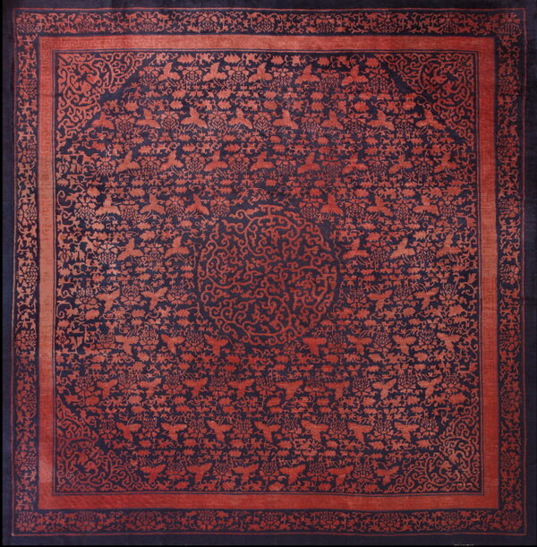 Square rug in deep indigo and rust red with dense floral, bird, and scrolling vine patterns.