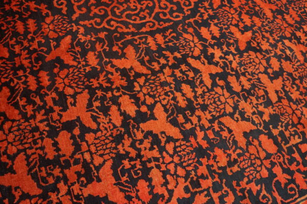 High-contrast orange and black rug pattern with intricate floral, vine, and scrollwork motifs.