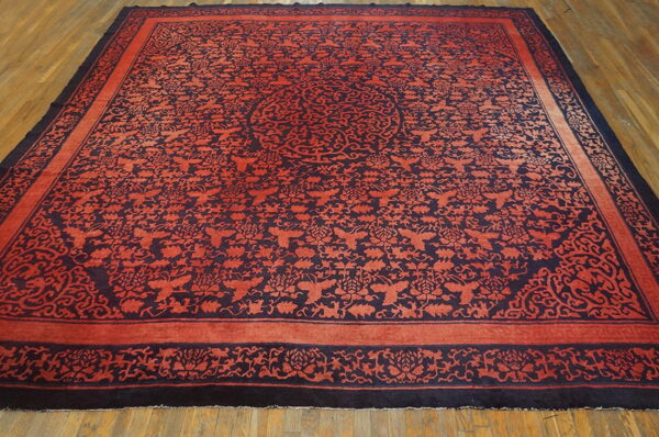 Square rug in terracotta and navy with intricate patterns and borders on light brown hardwood flooring.