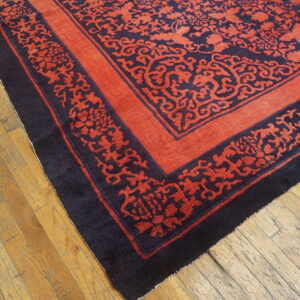 A terracotta rug with an intricate dark blue floral pattern and ornate border lies on worn wooden flooring.