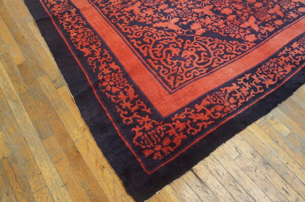A terracotta rug with an intricate dark blue floral pattern and ornate border lies on worn wooden flooring.