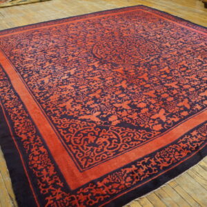 Large coral and dark blue rug with intricate scrollwork borders displayed on distressed wood floors.