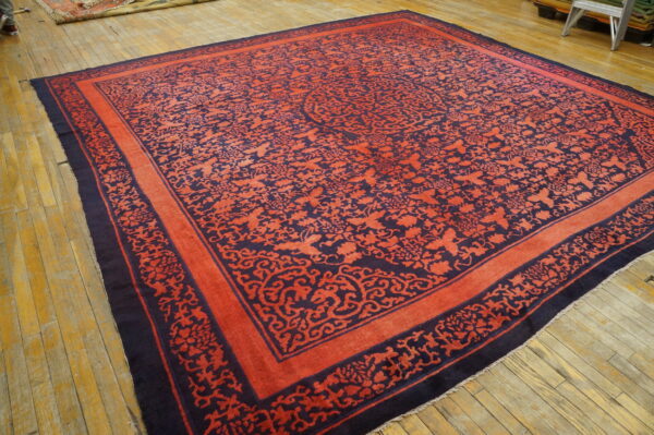 Large coral and dark blue rug with intricate scrollwork borders displayed on distressed wood floors.
