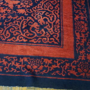 Navy and terracotta rug corner showing stylized scrolling floral borders on worn wood flooring.