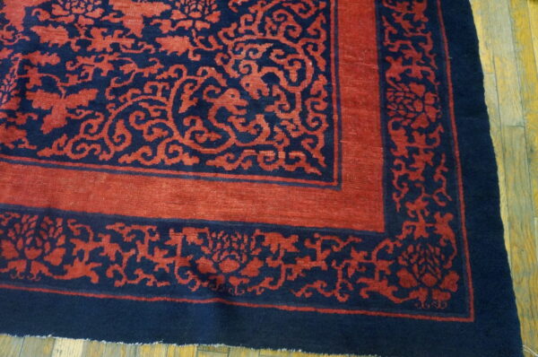 Navy and terracotta rug corner showing stylized scrolling floral borders on worn wood flooring.