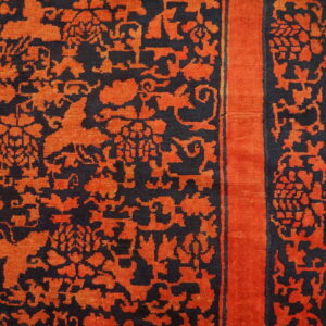 Black rug with bright orange floral patterns and a solid border lies on light wood flooring.