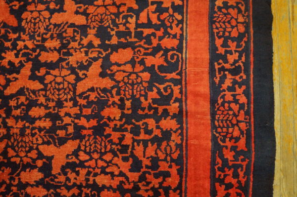 Black rug with bright orange floral patterns and a solid border lies on light wood flooring.