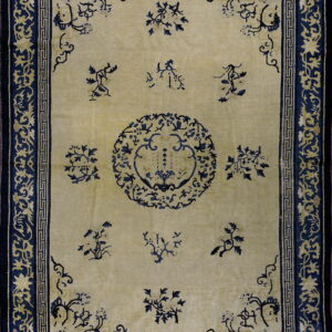 A traditional rug with a tan field and navy blue borders featuring floral and geometric motifs.
