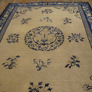 Light beige rug with navy stylized floral patterns and ornate borders on wooden plank flooring.