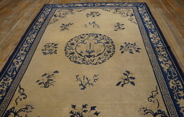Light beige rug with navy stylized floral patterns and ornate borders on wooden plank flooring.