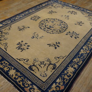 Beige rug featuring indigo blue floral sprays and geometric borders resting on distressed wooden plank flooring.