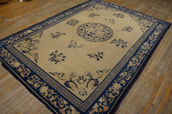 Beige rug featuring indigo blue floral sprays and geometric borders resting on distressed wooden plank flooring.